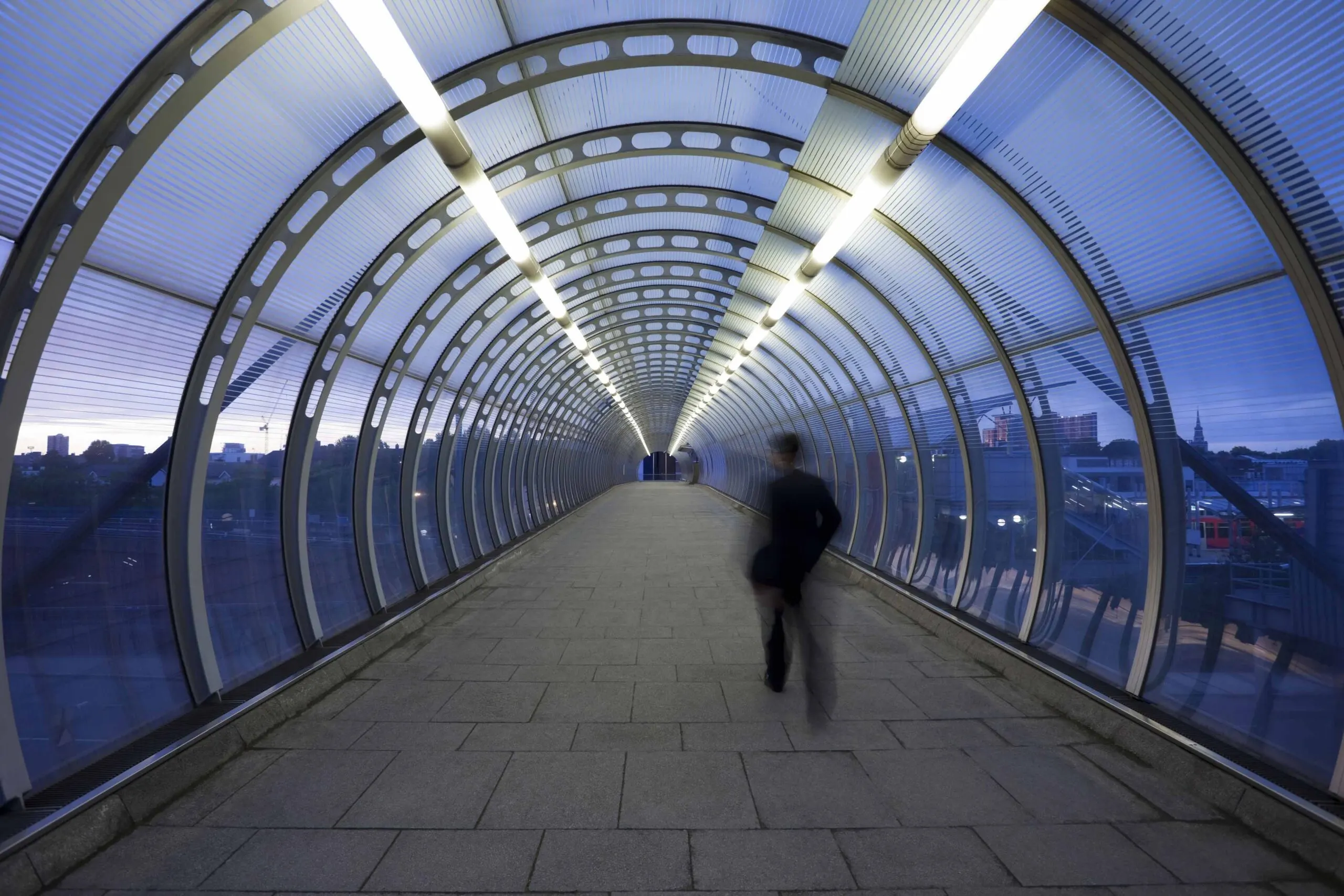 Businessman Walking Through Glass Skywalk at Twilight
